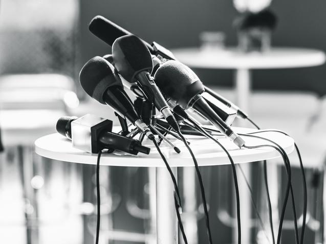 Mehrere Mikrofone in verschiedenen Größen stehen auf einem runden Tisch, Kabel sind verwirrt um die Ständer gewickelt.