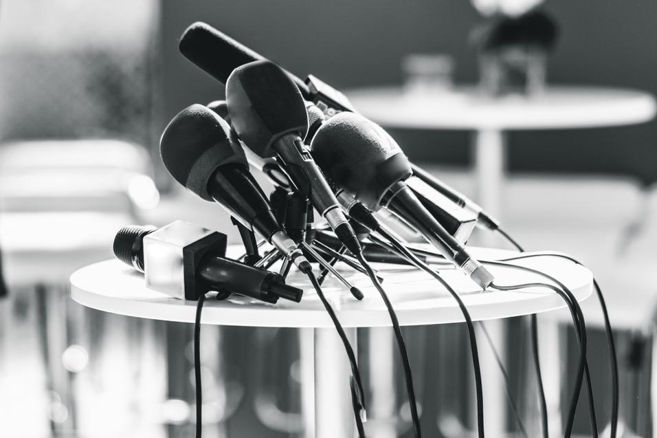 Mehrere Mikrofone in verschiedenen Gr&ouml;&szlig;en stehen auf einem runden Tisch, Kabel sind verwirrt um die St&auml;nder gewickelt.