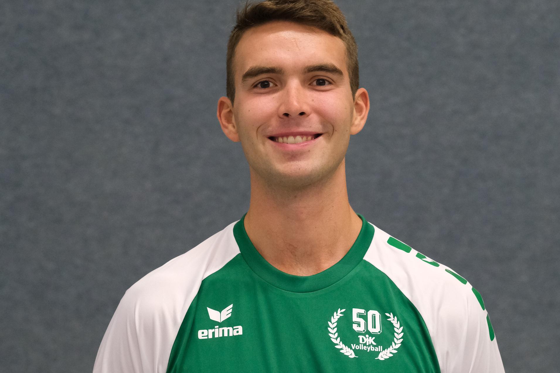 L&auml;chelnder Volleyballspieler in gr&uuml;nem Trikot mit Nummer 8, posing vor einem grauen Hintergrund.