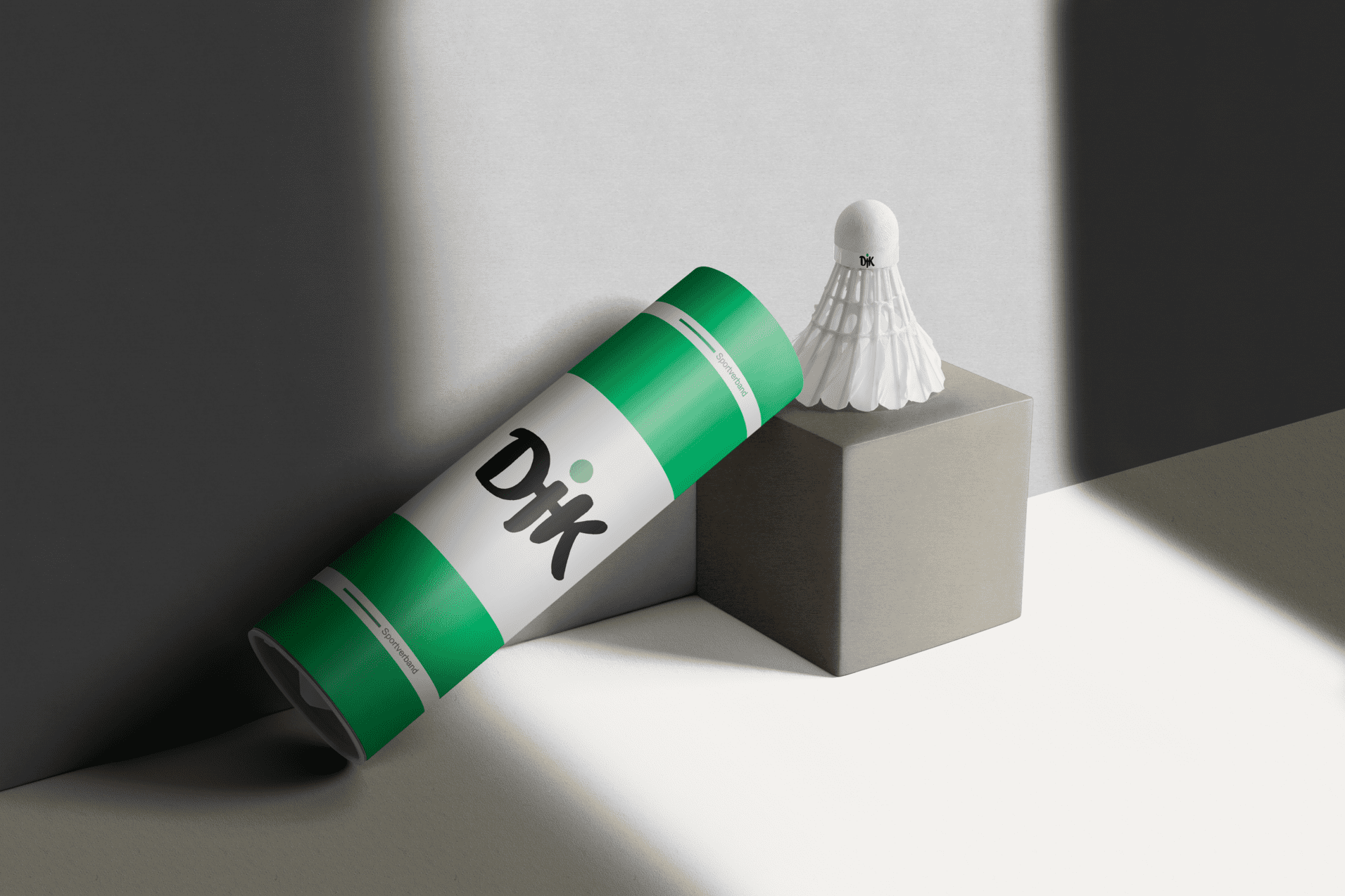Verpackung eines Badmintonschl&auml;gers steht neben einem Badmintonball auf einem grauen Block. Licht f&auml;llt auf die Szene.