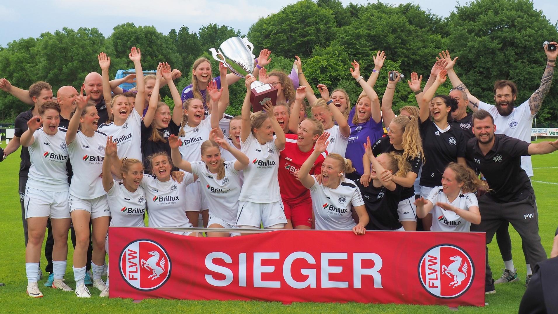 Mannschaft feiert mit Pokal und Banner "SIEGER" auf dem Fu&szlig;ballplatz, umgeben von jubelnden Spielerinnen und Unterst&uuml;tzern.