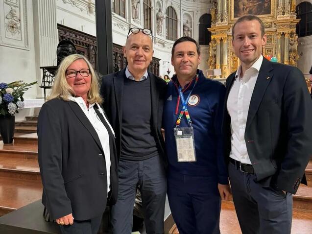 Vier Personen posieren in einer Kirche vor einem kunstvollen Altar. Helle, historische Architektur im Hintergrund.