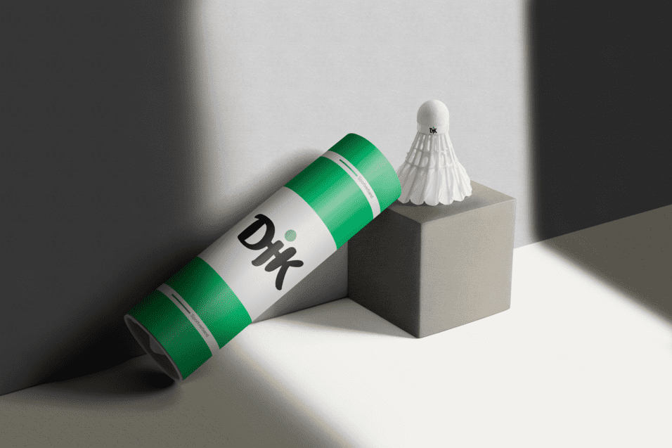 Verpackung eines Badmintonschl&auml;gers steht neben einem Badmintonball auf einem grauen Block. Licht f&auml;llt auf die Szene.