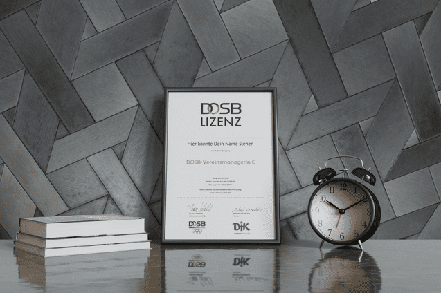 Rahmen mit DOSB-Lizenz-Zertifikat auf einem Tisch, daneben ein Wecker und Stapel B&uuml;cher vor gestreifter Wand.