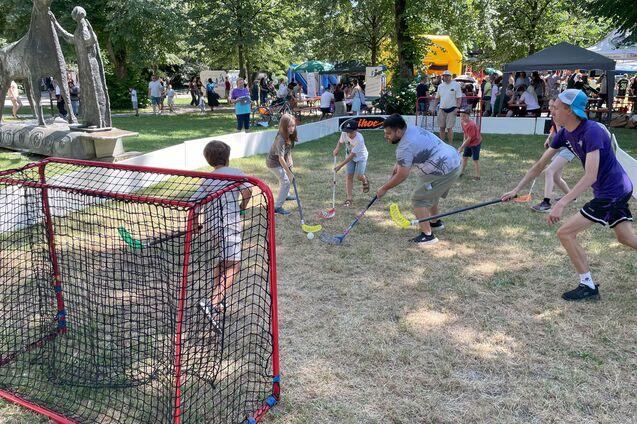 Kinder und Erwachsene spielen mit Schl&auml;gern und bunten B&auml;llen in der N&auml;he eines Fu&szlig;balltores im Freien.