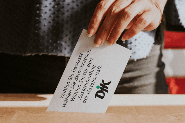 Hand einer Person, die eine Wahlkarte in eine Box einwirft, mit Text &uuml;ber bewusstes W&auml;hlen und Demokratie.