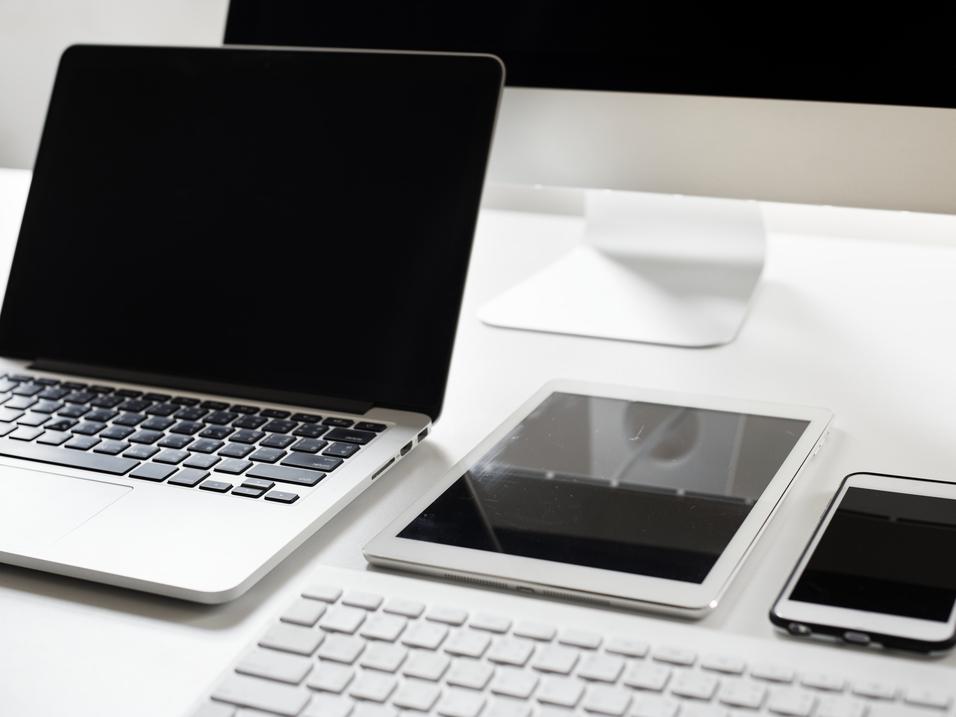 Moderne Arbeitsstation mit einem Laptop, Tablet und Smartphone auf einem wei&szlig;en Tisch. Tastatur ebenfalls sichtbar.