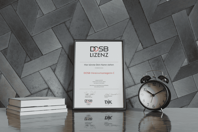 Rahmen mit DOSB-Lizenz-Zertifikat auf einem Tisch, daneben ein Wecker und Stapel B&uuml;cher vor gestreifter Wand.