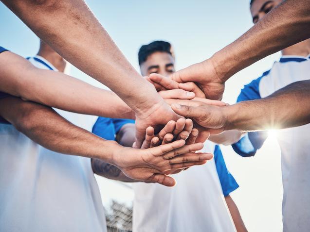 F&uuml;nf H&auml;nde von Fu&szlig;ballspielern legen sich in der Mitte zusammen, symbolisieren Teamgeist und Zusammenhalt.