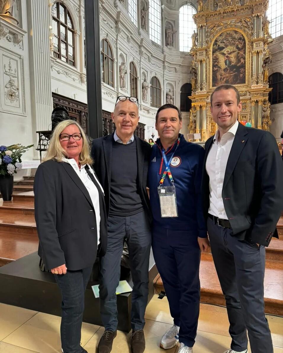 Vier Personen posieren in einer Kirche vor einem kunstvollen Altar. Helle, historische Architektur im Hintergrund.