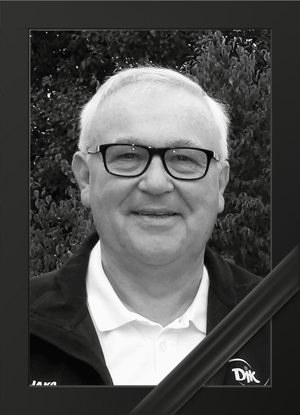 Schwarz-wei&szlig;e Portraitaufnahme eines &auml;lteren Mannes mit Brille, l&auml;chelnd vor einem gr&uuml;nen Hintergrund.