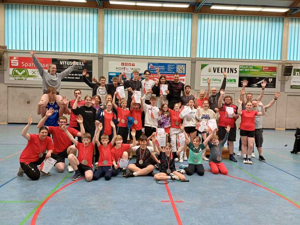 Gruppenfoto von 40 Personen in Sportkleidung, die jubelnd mit Urkunden in einer Sporthalle stehen.