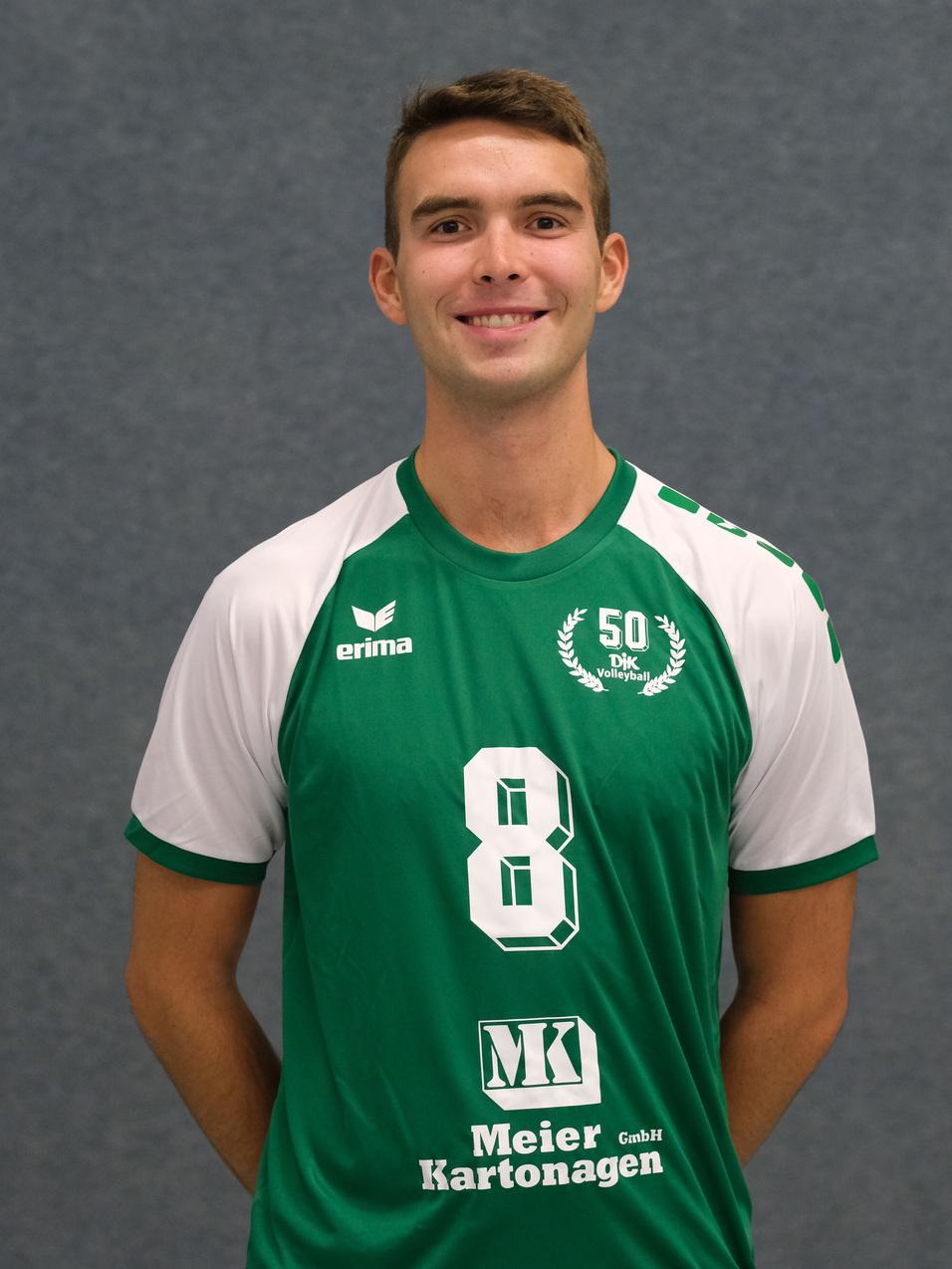 L&auml;chelnder Volleyballspieler in gr&uuml;nem Trikot mit Nummer 8, posing vor einem grauen Hintergrund.