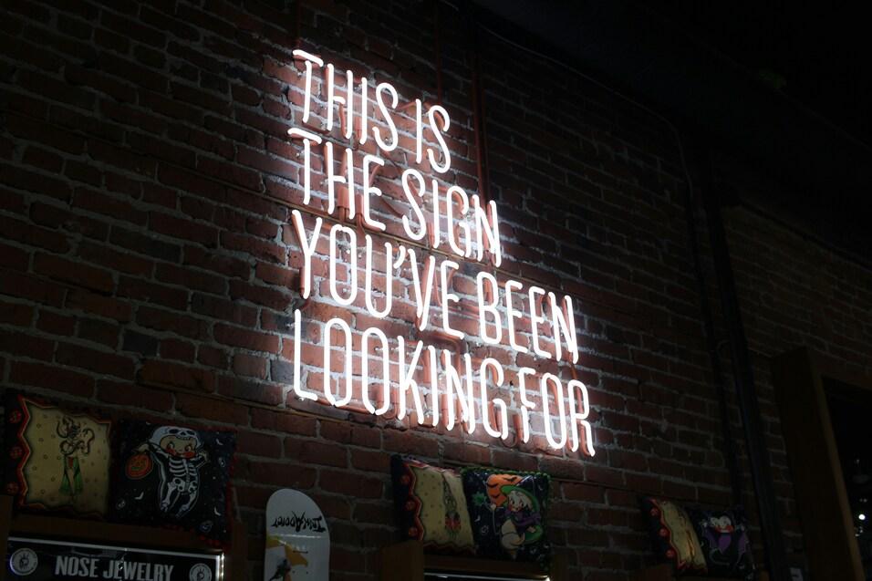 Neonlicht mit der Aufschrift &bdquo;THIS IS THE SIGN YOU'VE BEEN LOOKING FOR&ldquo; an einer Ziegelwand.