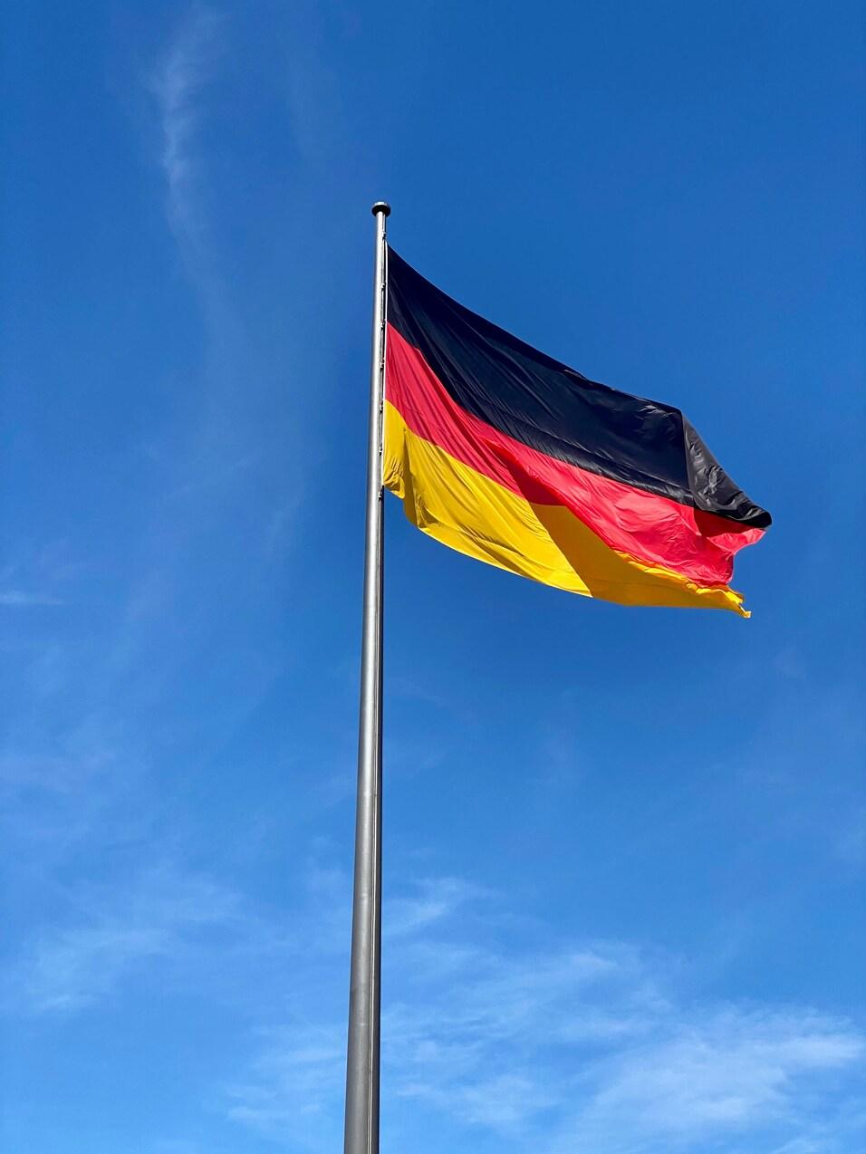 Flagge Deutschlands weht vor blauem Himmel, schwarz-rot-goldene Streifen sind deutlich zu erkennen.
