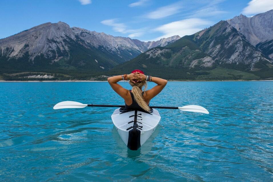Frau sitzt im Kajak auf klarem, turquoise Wasser mit Bergen im Hintergrund und genie&szlig;t die Aussicht.