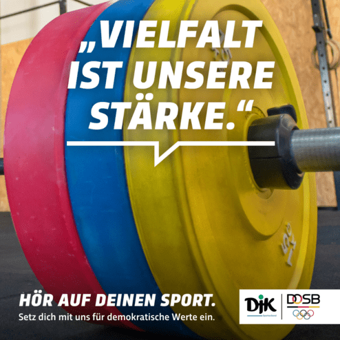 Nahaufnahme einer Hantel mit bunten Gewichten und dem Slogan &bdquo;Vielfalt ist unsere St&auml;rke&ldquo; im Hintergrund.