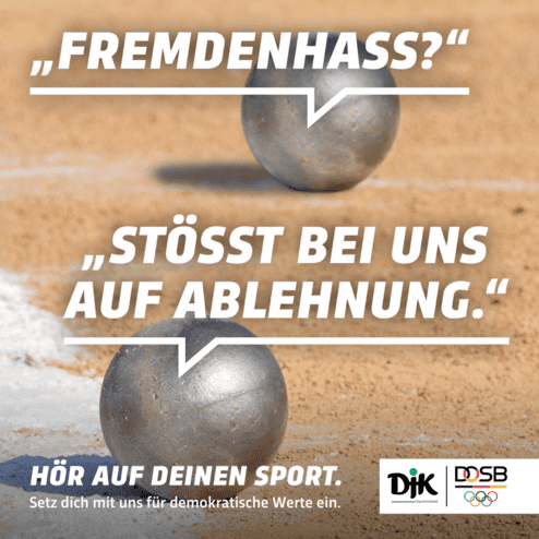 Silberne Kugeln liegen auf einem Sandplatz, mit Text &uuml;ber Fremdenhass und Ablehnung im Hintergrund.