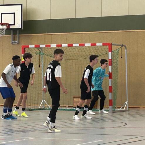 F&uuml;nf Jugendliche stehen in einer Sporthalle vor einem Tor, bereit zum Fu&szlig;ballspielen.