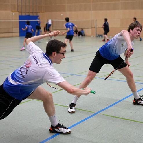 Zwei Jugendliche spielen Badminton in einem Sporthallen-Setting, w&auml;hrend sie den Federball zuspielen.