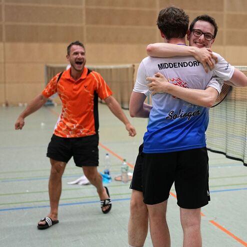 Drei Tischtennisspieler feiern einen Sieg, zwei umarmen sich, w&auml;hrend einer im Hintergrund jubelt.