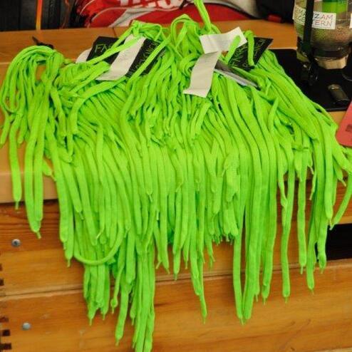 Bunte gr&uuml;ne Sportschn&uuml;rsenkel liegen zusammen auf einem Holztisch, teilweise mit Preisschildern versehen.