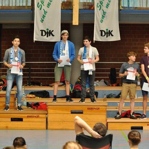 F&uuml;nf Jugendliche stehen auf Podesten und halten Urkunden bei einer Sportveranstaltung in einer Halle.