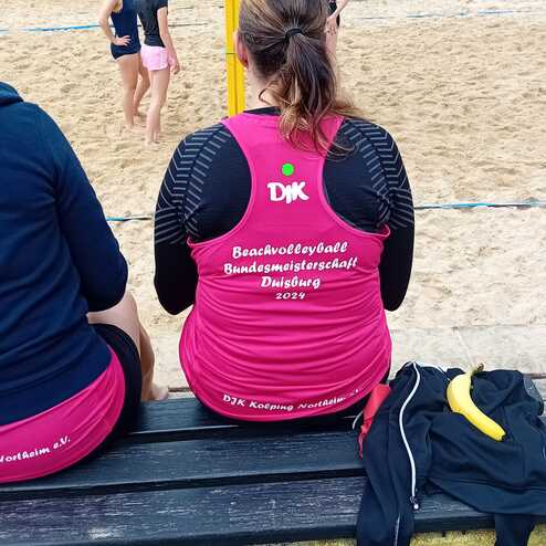 R&uuml;ckansicht einer Person in pinkem Trikot mit der Aufschrift &bdquo;Beachvolleyball Bundesmeisterschaft Duisburg 2024&ldquo;.