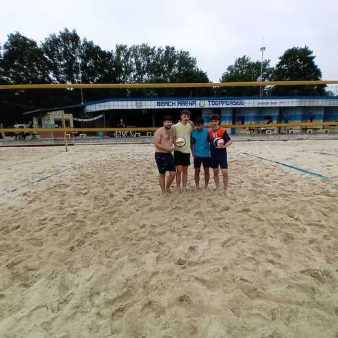 Drei Personen stehen auf einem Sandstrandvolleyballplatz und halten einen Volleyball und einen Beachball.