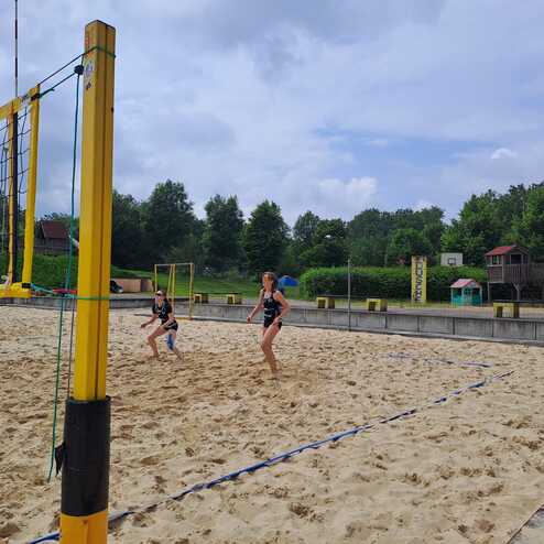 Zwei Kinder spielen Beachvolleyball auf einem Sandplatz unter einem bew&ouml;lkten Himmel.