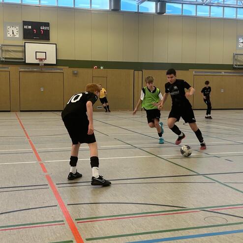 Drei Fu&szlig;ballspieler in Sportkleidung dribbeln einen Ball auf einem Hallenfu&szlig;ballfeld.