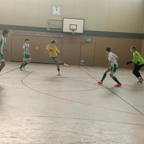 F&uuml;nf Jugendfu&szlig;ballspieler im Spiel, ein Spieler schie&szlig;t auf das Tor, ein Torwart bereit zur Abwehr.