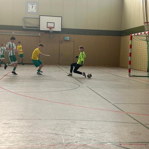 F&uuml;nf Jugendliche spielen in einer Sporthalle Fu&szlig;ball, ein Torwart bereitet sich auf einen Schuss vor.
