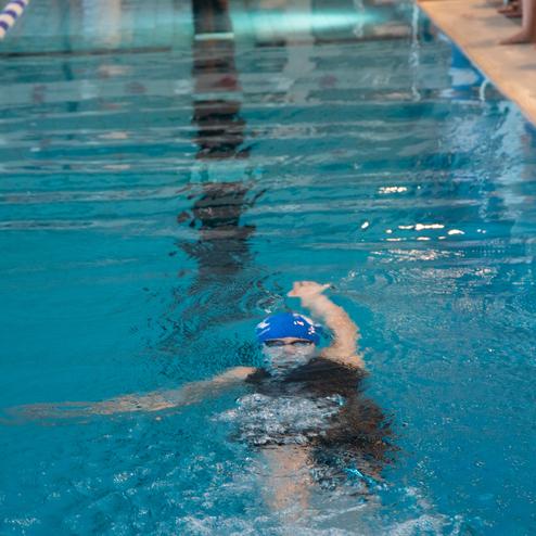 Schwimmerin mit blauer Schwimmhaube trainiert im klaren Wasser eines Schwimmbeckens. Zuschauer stehen am Rand.