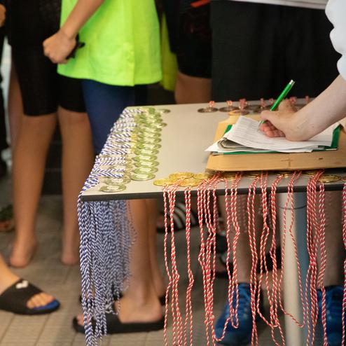 Tisch mit Medaillen und Notizen, umgeben von schwimmenden Jugendlichen in Wettkampfkleidung.
