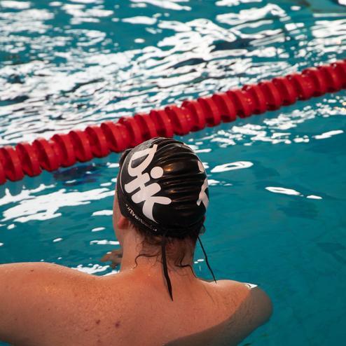 Nahaufnahme einer Schwimmerin mit schwarzer Badekappe, die im Becken neben einem roten Schwimmbahn-Seil steht.