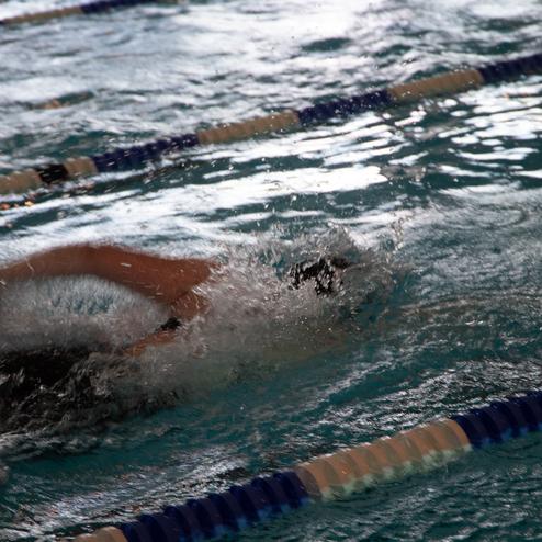 Schwimmer in Aktion, der mit einem Arm in einem Becken schwimmt, Wasser spritzt auf.