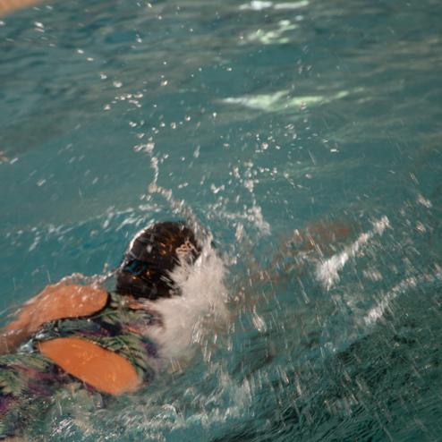 Junge Schwimmerin taucht mit Kopf unter Wasser, spritzt Wasser auf einer Bahn in einem Hallenbad.