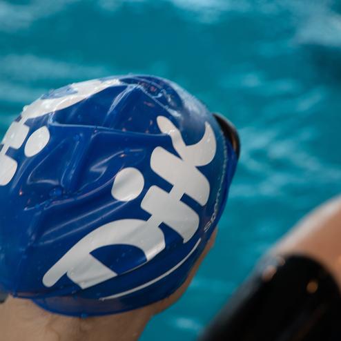 Blick auf einen Schwimmer mit blauer Badekappe, der am Beckenrand auf das Wasser blickt.