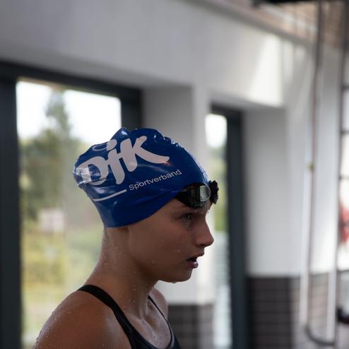 Junge Schwimmerin mit blauer Badekappe und Schwimmbrille, bereit f&uuml;r den Wettkampf in einem Schwimmbad.