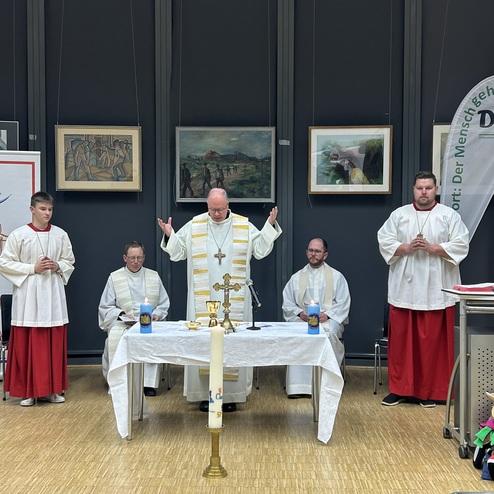 Vier Ministranten und ein Priester stehen um einen Altar mit Kerzen, w&auml;hrend sie einen Gottesdienst feiern.