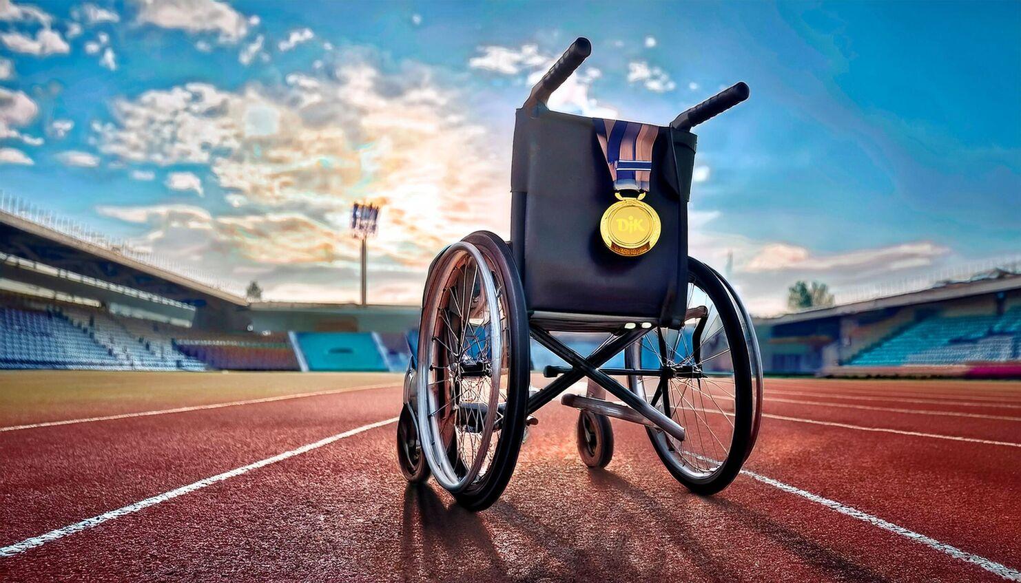 Rollstuhl mit Goldmedaille steht auf einer Laufbahn im Stadion, im Hintergrund der Himmel mit Wolken.