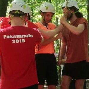 Gruppenszene im Wald: Vier Personen mit Helmen stehen zusammen, um eine Team&uuml;bung durchzuf&uuml;hren.