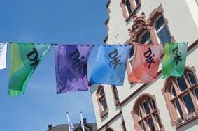 Bunte Fahnen mit chinesischen Schriftzeichen h&auml;ngen vor einer historischen Geb&auml;udefassade unter blauem Himmel.