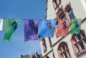 Bunte Fahnen mit chinesischen Schriftzeichen h&auml;ngen vor einer historischen Geb&auml;udefassade unter blauem Himmel.