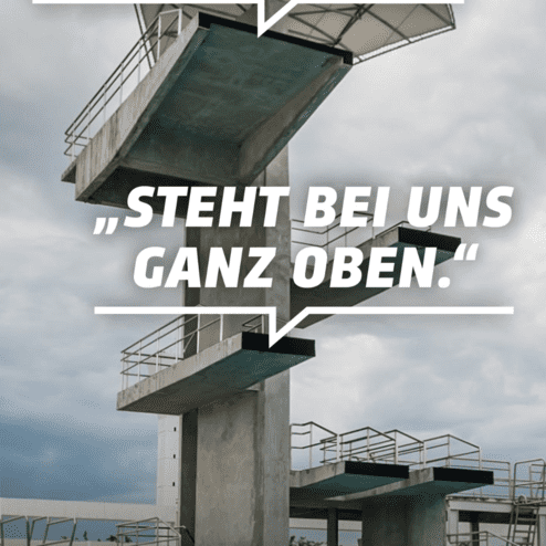 Blick auf ein Sprungbrett eines Schwimmbads, dar&uuml;ber graue Wolken und Text&uuml;berlagerungen mit demokratischen Botschaften.