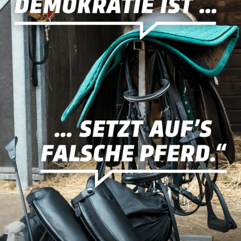 Sattel und Reitstiefel stehen in einem Stall, mit einem Zitat &uuml;ber Demokratie im Vordergrund.