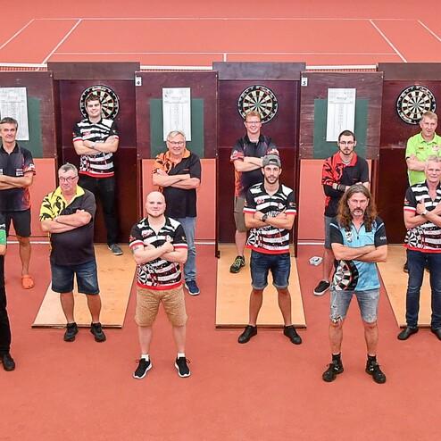 Gruppenszene von Dartspielern, die in der Mitte einer Sporthalle vor Dartboards stehen und posieren.