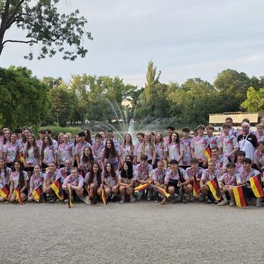 Gruppenfoto von Jugendlichen mit Deutschlandfahnen in einem Park vor einem Springbrunnen.