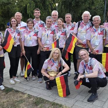 Gruppe von Menschen in bunten Shirt mit deutschen Flaggen, die lächeln und auf einem Gehweg stehen.